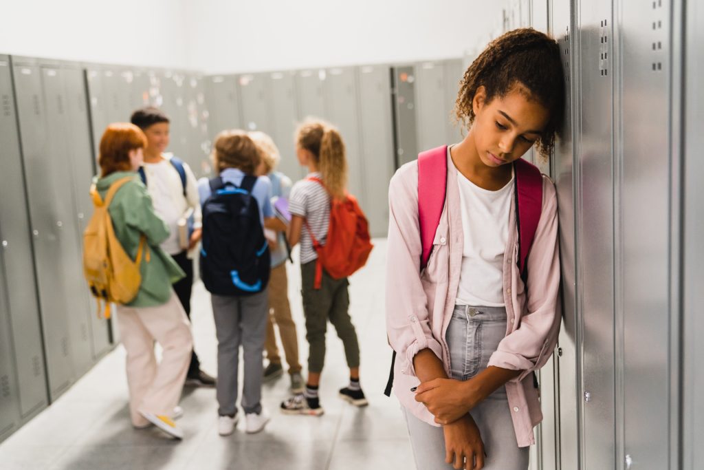 Lonely sad schoolgirl crying while all her classmates are ignoring her.