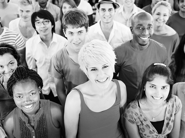 Black and white photo of a diverse group of smiling people looking at the camera. They range in age, gender, and ethnicity, showcasing unity and diversity.