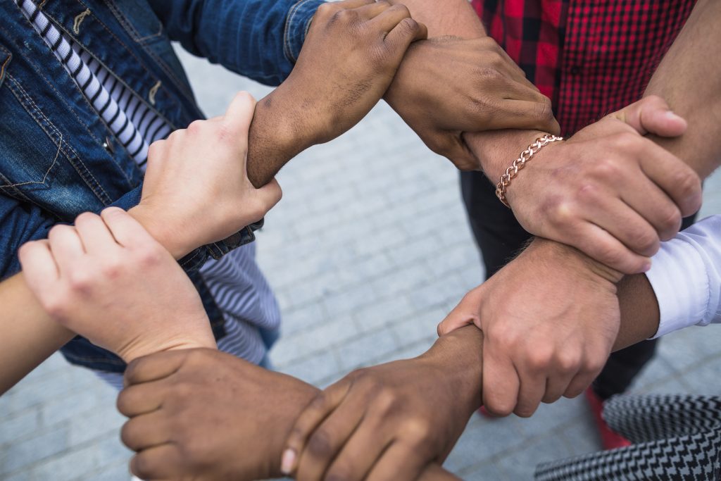 Close-up of multiple hands of diverse skin tones clasping each other in a gesture of connection.