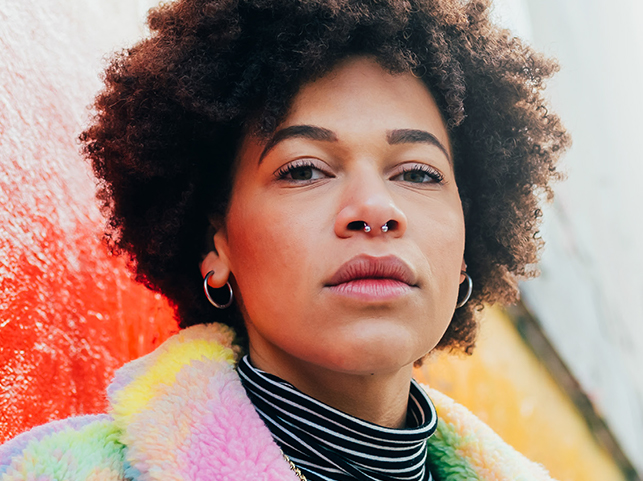 A close-up of a woman with curly hair and a colorful jacket, looking introspective.