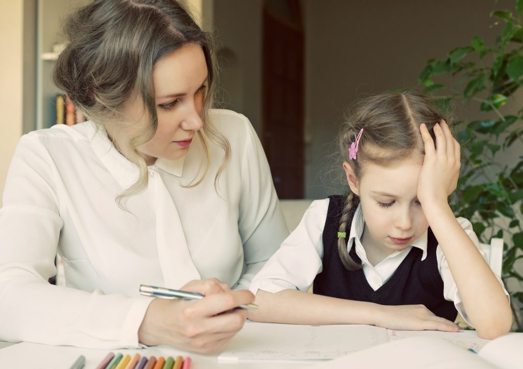 Mother helping her tired daughter with homework at home.