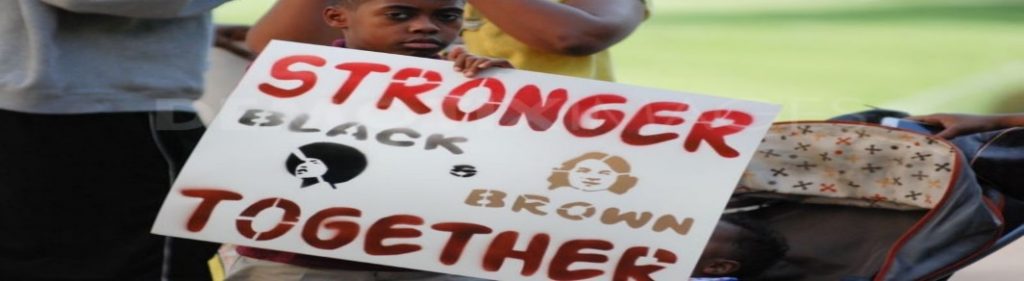 A young boy holding sign that reads “Stronger Black Brown Together”.