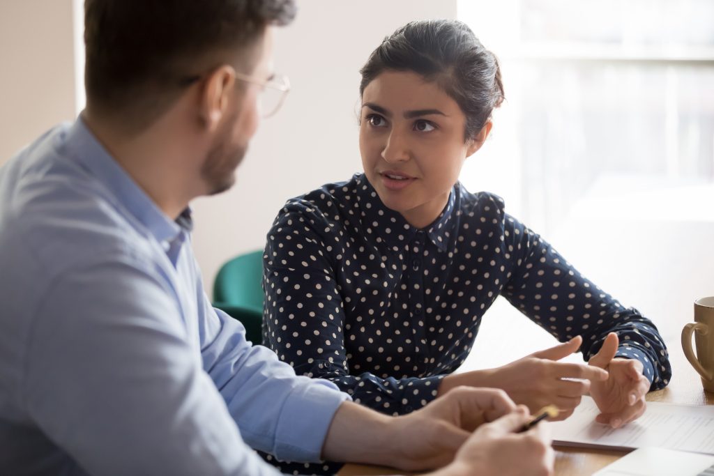 Young female talking to listening male at a desk.