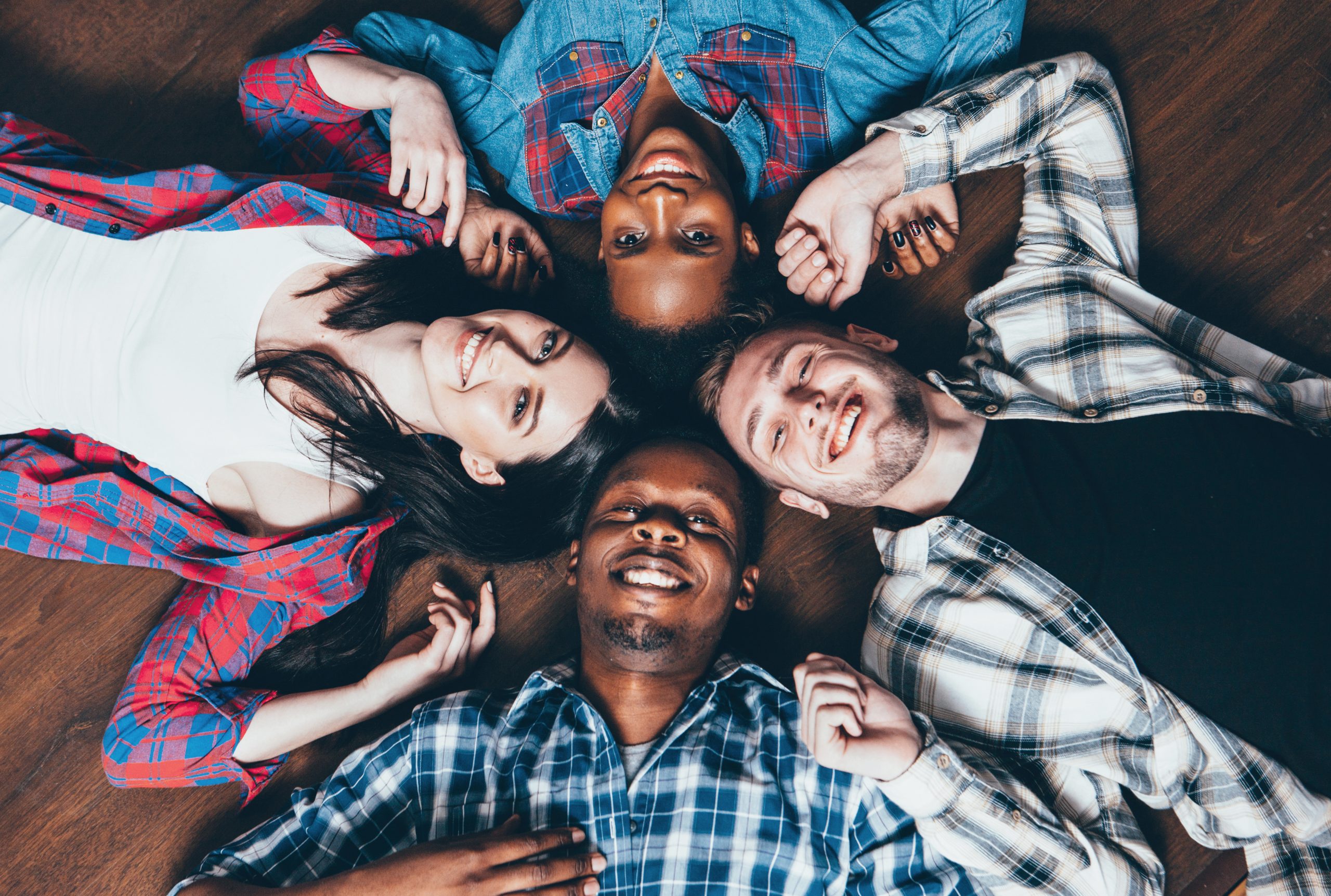 Four friends of diverse backgrounds lying in a circle with their heads touching at the center.