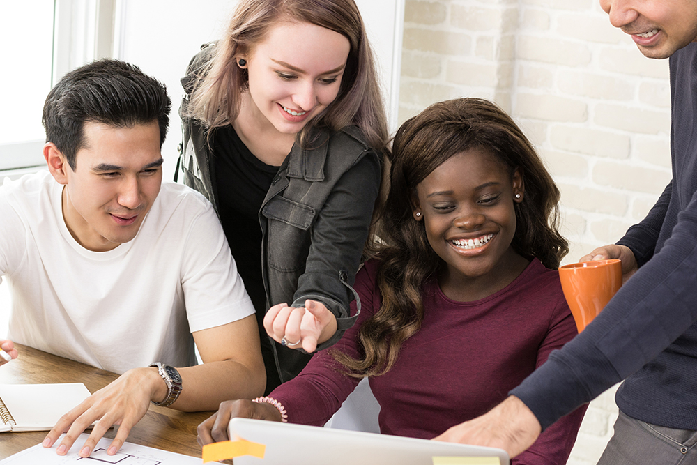 Group of diverse students around a computer going through the how to be a safe supportive person presentation.